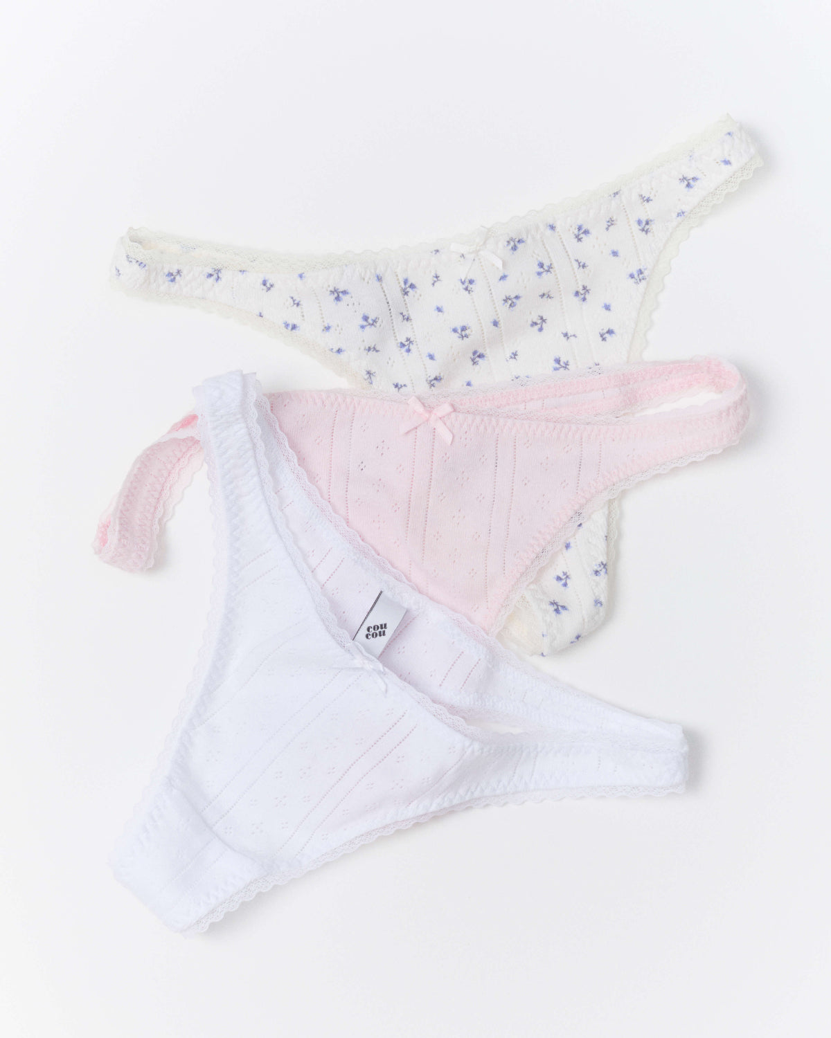 Three pairs of women's underwear laid flat on a white background: a white pair with a small blue floral print, a light pink pair with a tiny bow, and a white pair.