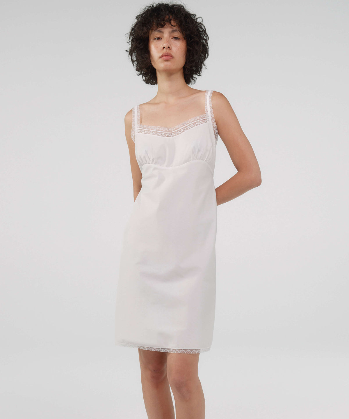 Woman wearing a white slip dress against a plain background