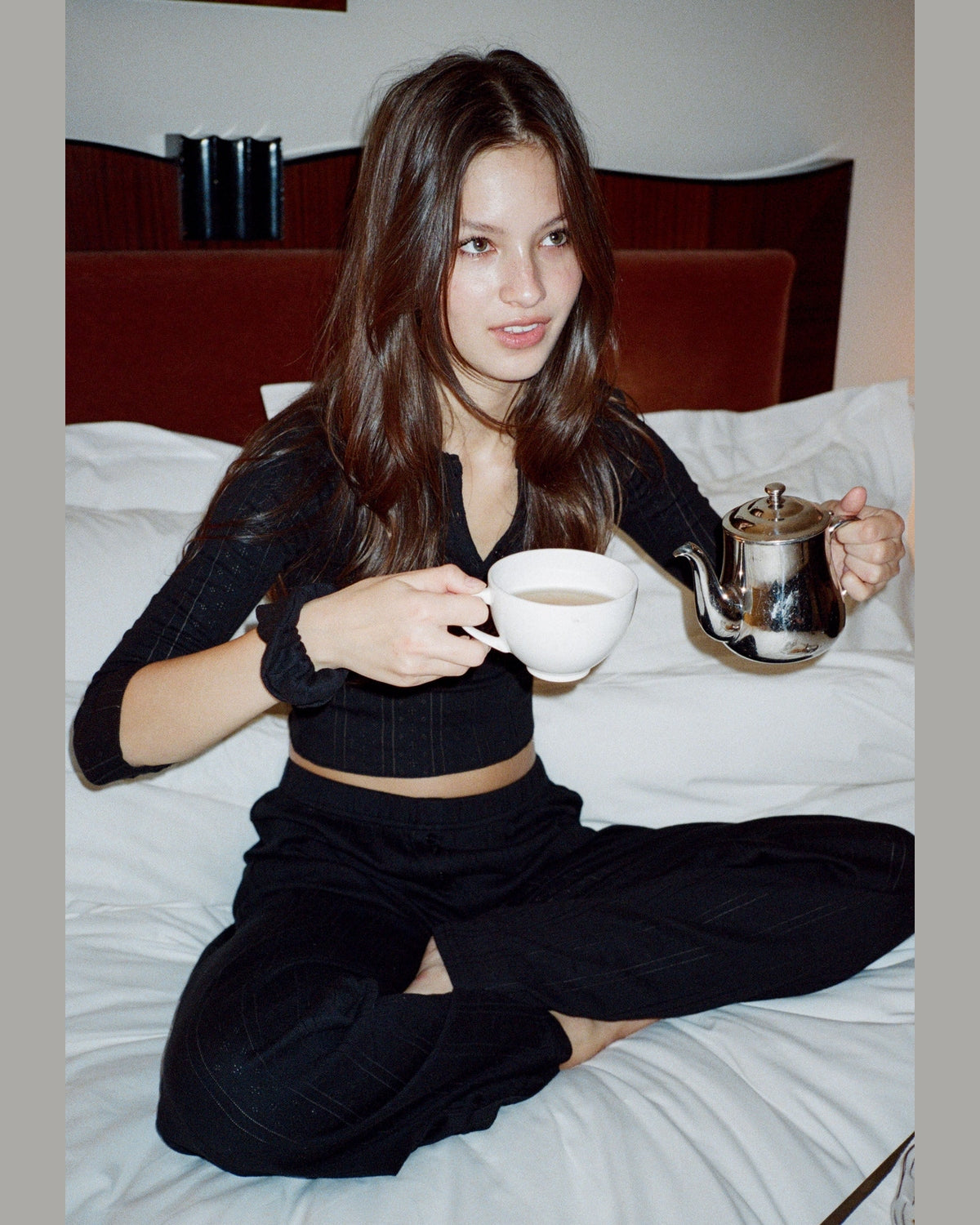 Woman sitting on a bed holding a teacup and teapot