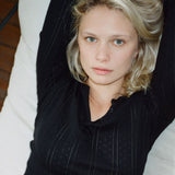 Woman with blonde hair wearing a black pinstripe shirt sitting on a white couch.