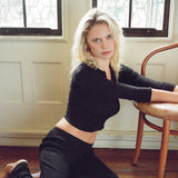 Woman in black outfit sitting on a wooden floor with a chair in the background