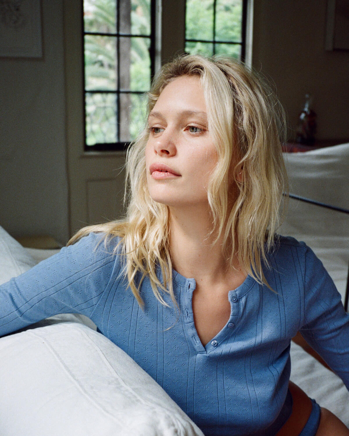 Woman in a blue shirt sitting on a bed in a softly lit room.