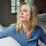 Woman in a blue shirt sitting on a bed in a softly lit room.