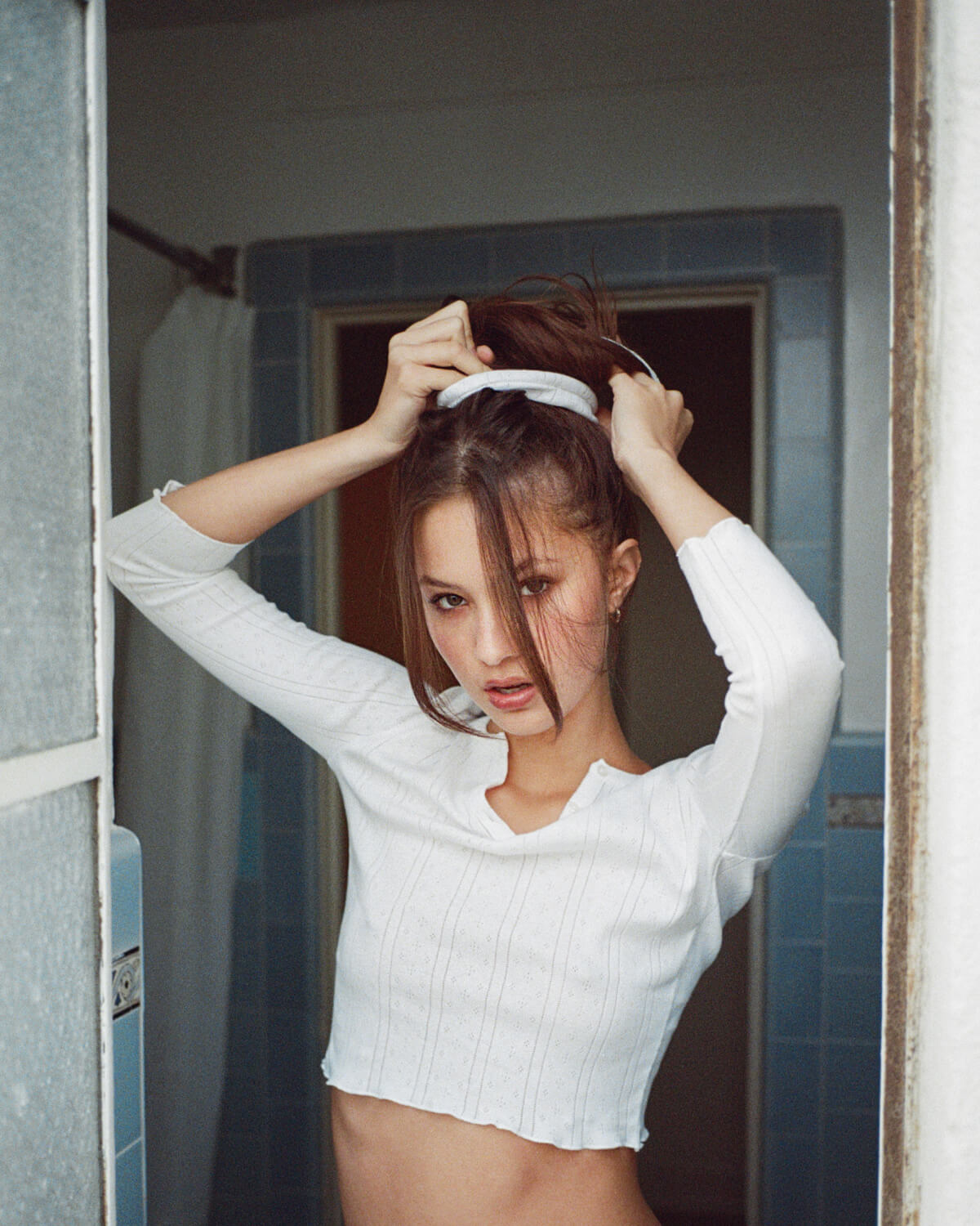 Woman in a white long-sleeve top standing in a bathroom.