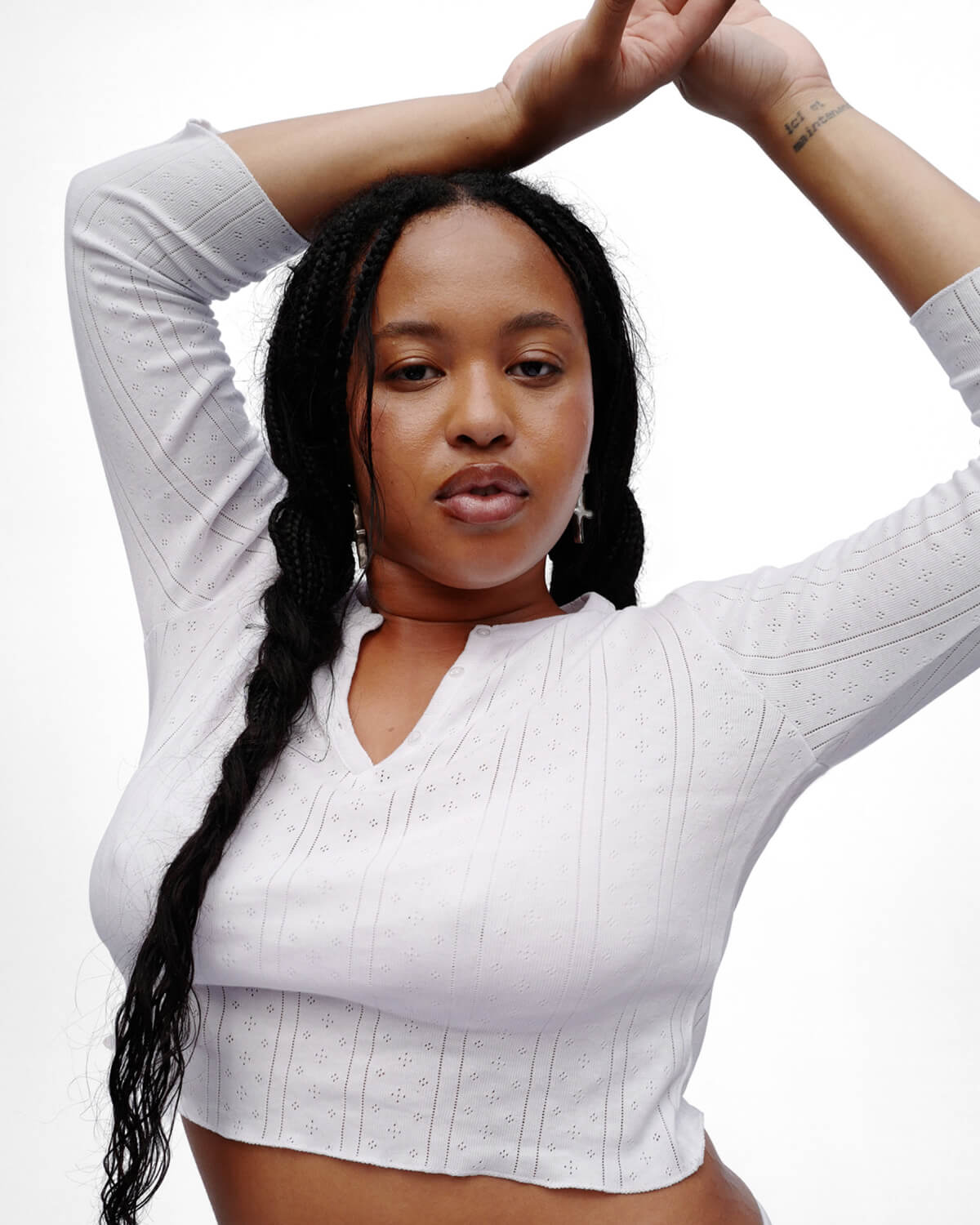 Woman wearing a white ribbed crop top with long braided hair on a white background