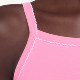 Close-up of a model wearing a bright pink ribbed tank top with delicate white scalloped trim along the neckline and straps.