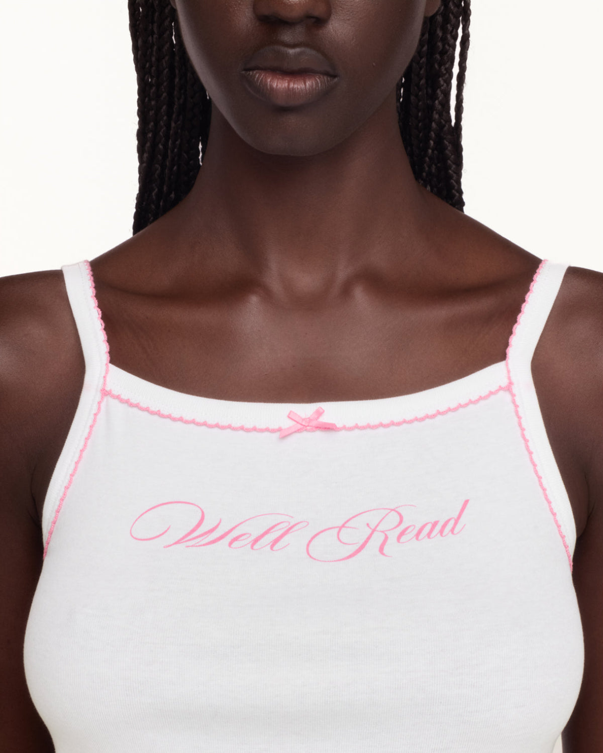 A close-up of a model wearing a white camisole tank top with pink trim and 'Well Read' embroidered in pink script across the chest.