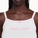 A close-up of a model wearing a white camisole tank top with pink trim and 'Well Read' embroidered in pink script across the chest.
