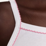 Close-up of a white ribbed tank top with pink trim along the neckline, worn by a model.