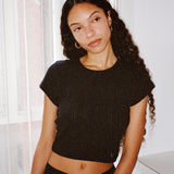Woman wearing a black crop top and black shorts indoors with white curtains in the background