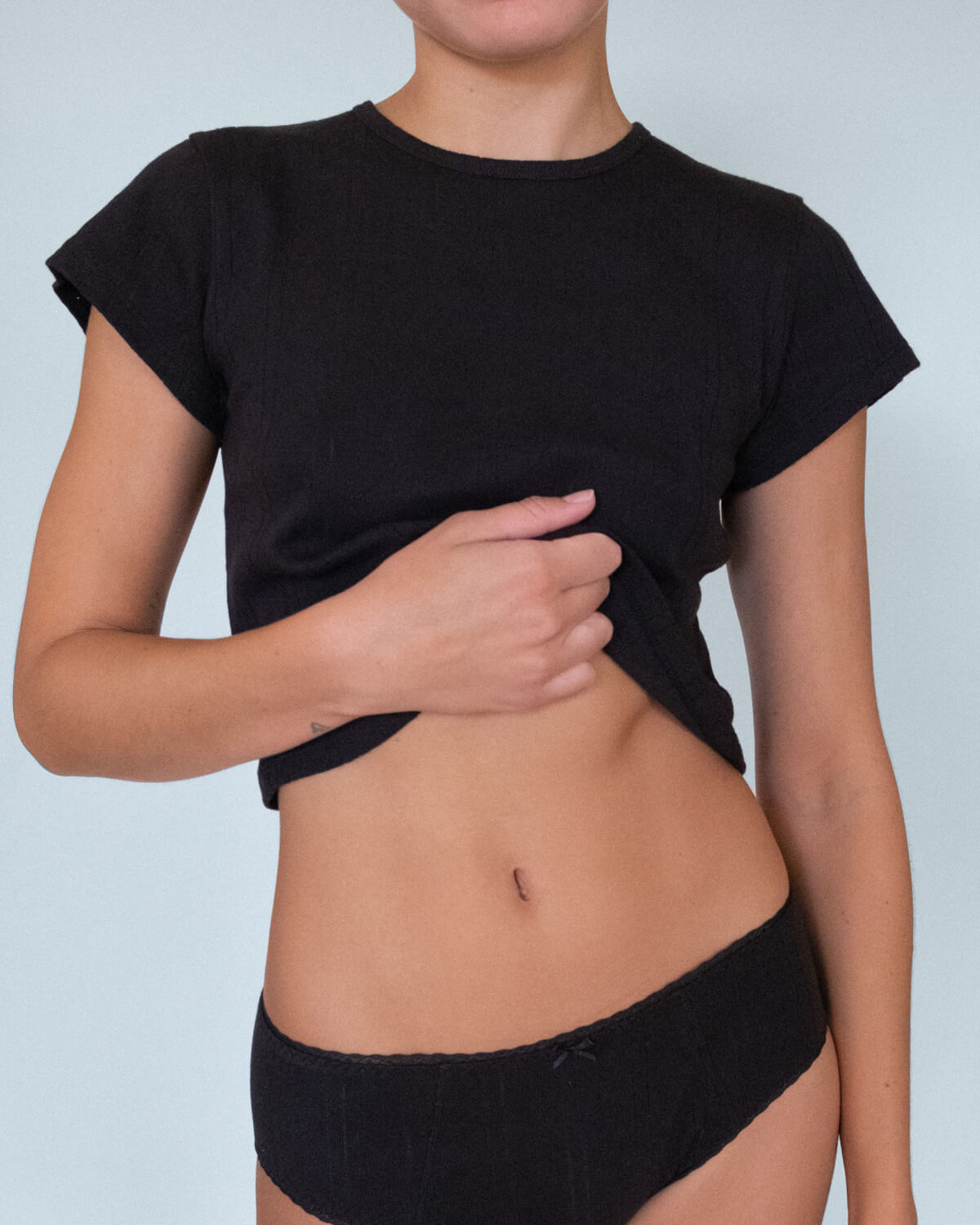 Person wearing a black crop top and black underwear against a light blue background
