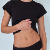 Person wearing a black crop top and black underwear against a light blue background