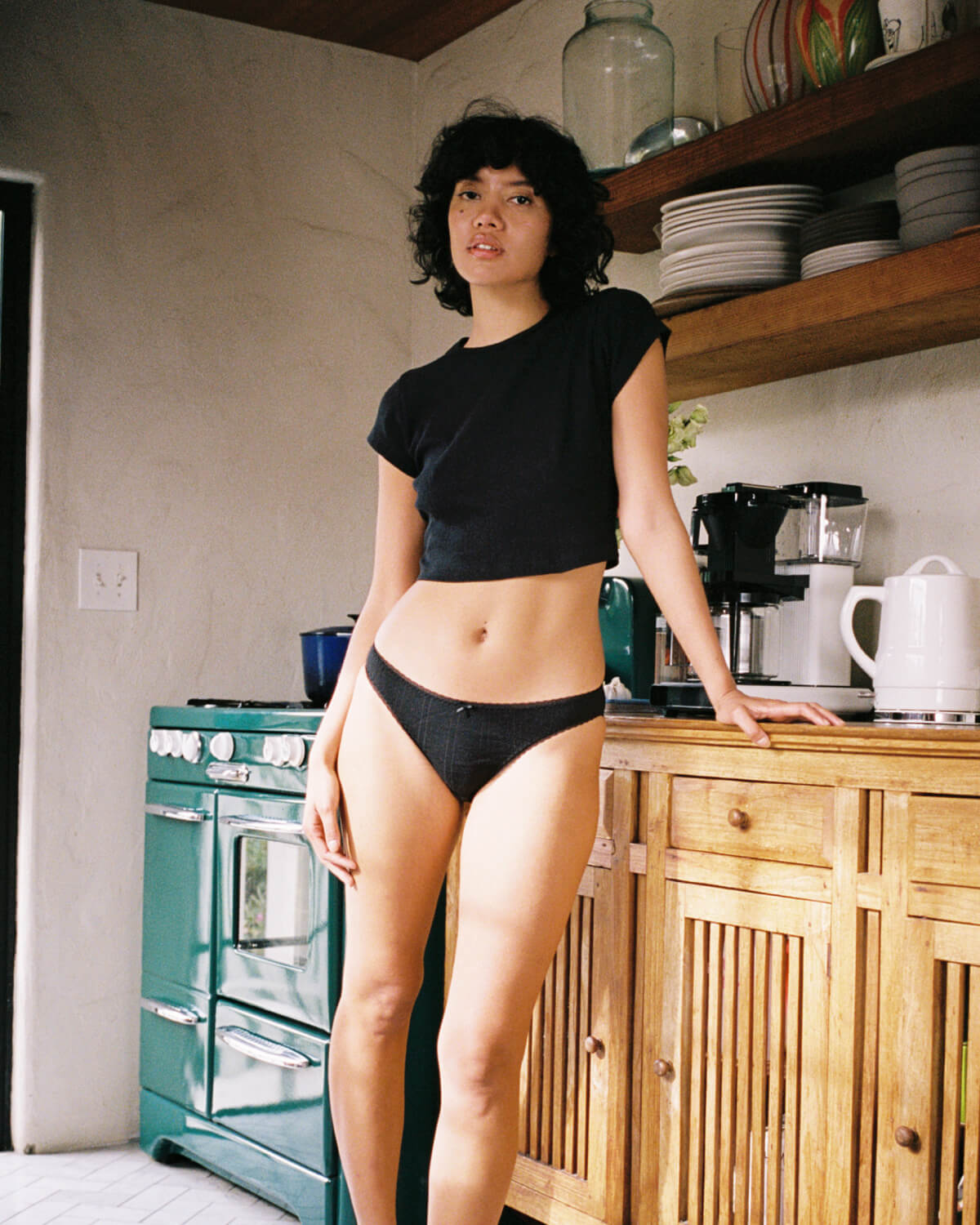 Person wearing a black top and underwear in a kitchen.