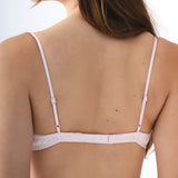 Woman wearing a light pink bralette with thin straps on a white background