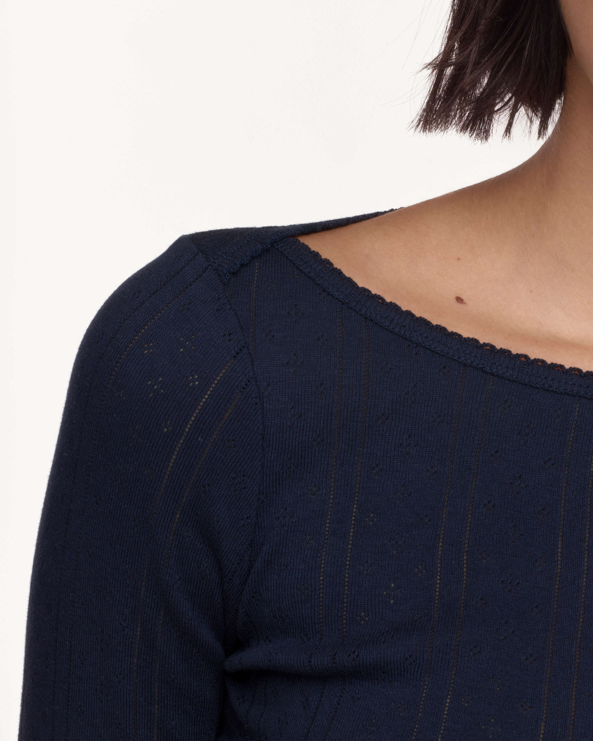 Close-up of a person wearing a dark navy textured knit top with a scalloped neckline, against a plain light background.