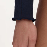 Close-up of a person's hand and forearm wearing a dark navy ribbed knit sleeve with a scalloped cuff, against a plain light background.