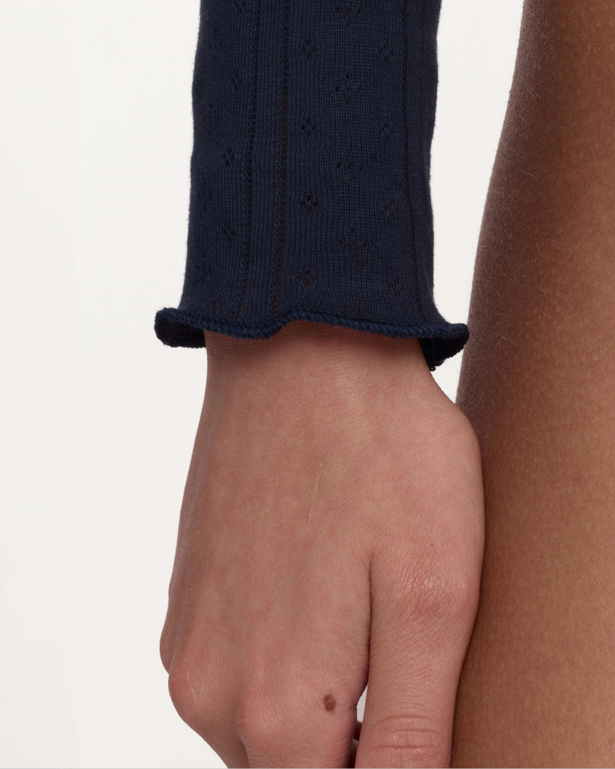 Close-up of a person's hand and forearm wearing a dark navy ribbed knit sleeve with a scalloped cuff, against a plain light background.