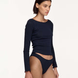 A model wearing a dark navy blue ribbed long-sleeve crop top and matching high-cut underwear, photographed against a clean off-white studio background.