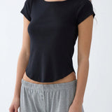 A woman wearing a black short-sleeve scoop-neck top and gray sweatpants, shown from the neck down against a plain light background.