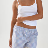 Woman wearing a white tank top and blue checkered shorts on a plain background