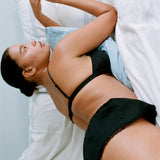 Woman lying on a bed wearing a black bra and panties.