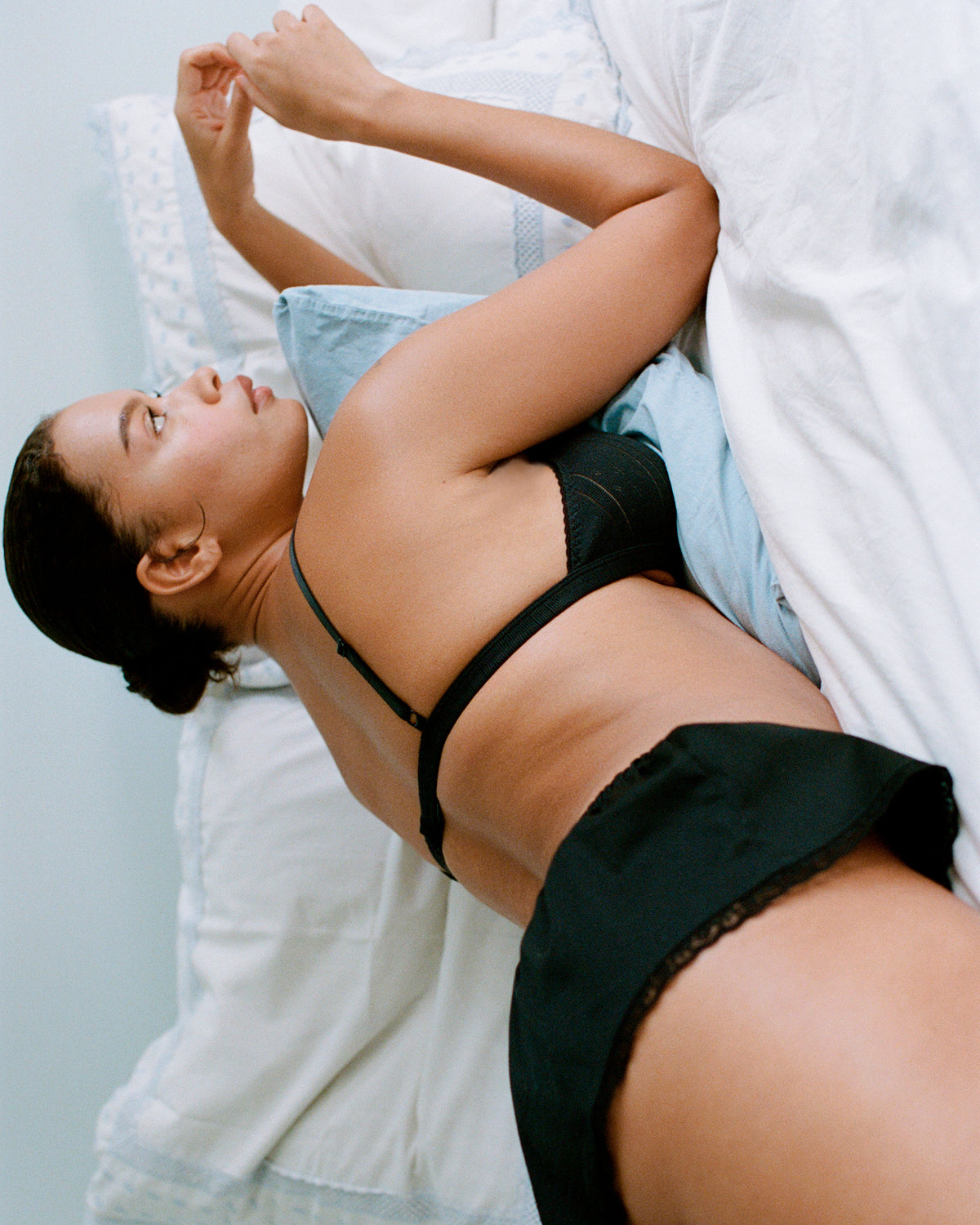 Woman lying on a bed wearing a black bra and panties.