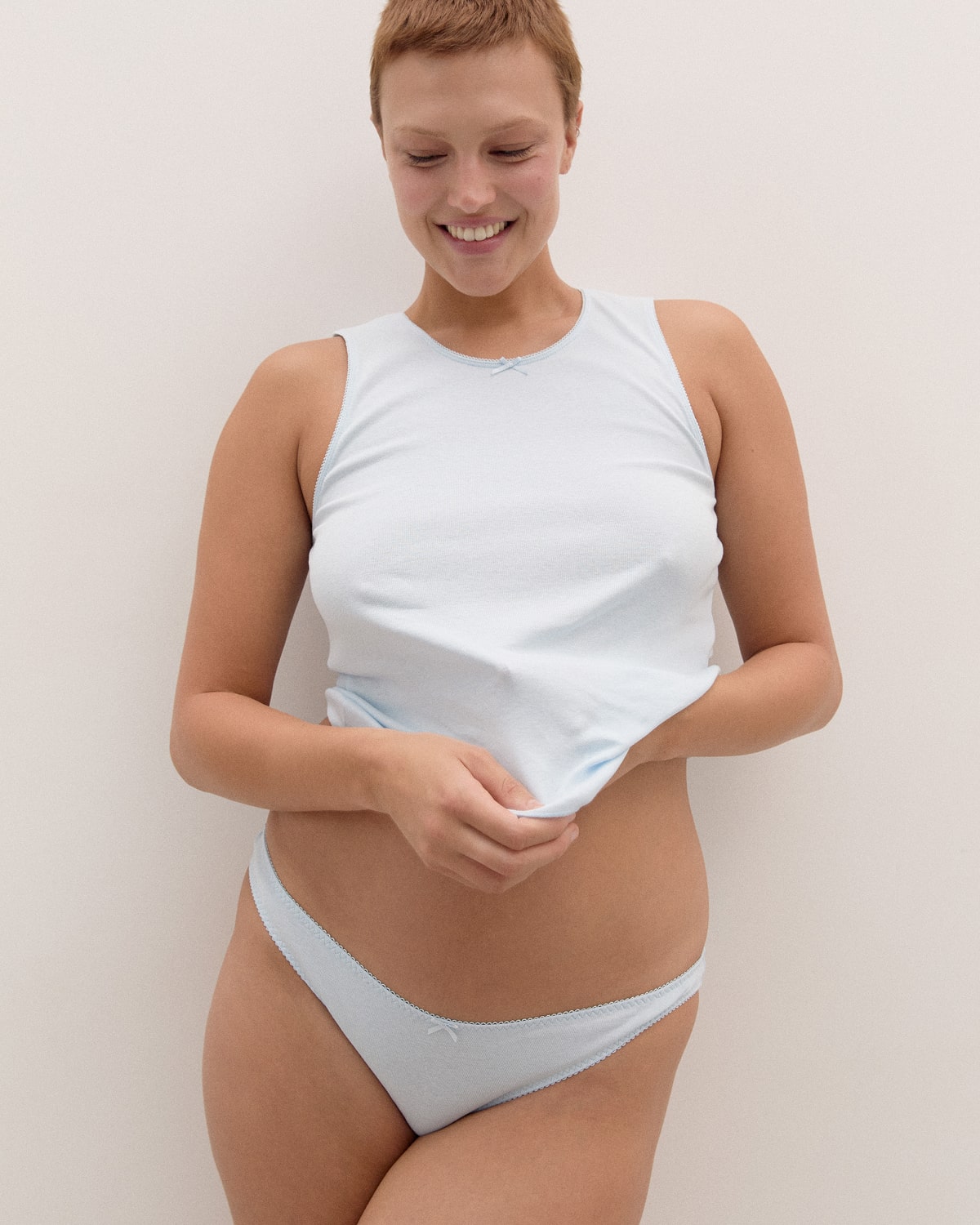 Woman wearing a light blue vest and briefs against a plain background