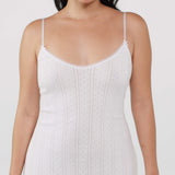 Woman wearing a white slip dress with thin straps on a plain background