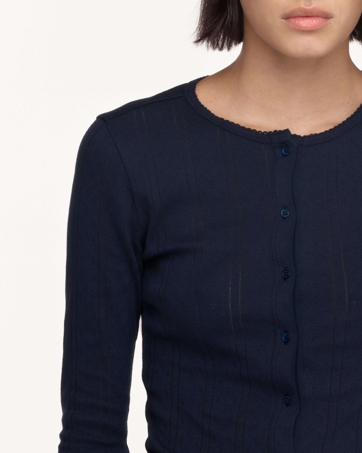 Close-up of a model wearing a dark navy ribbed knit long-sleeve top with a buttoned front and scalloped neckline.