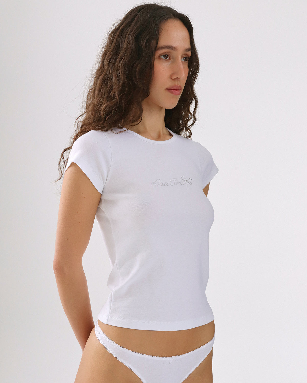 Woman wearing a white t-shirt and white underwear against a plain background