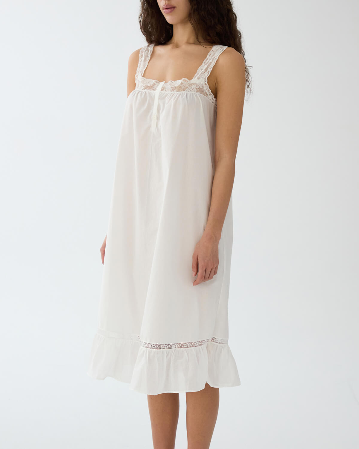 Woman wearing a white nightgown with lace details on a plain background