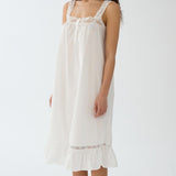 Woman wearing a white nightgown with lace details on a plain background