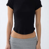 A woman wearing a black short-sleeve boat-neck crop top and gray athletic shorts, shown from the neck down against a plain light gray background.