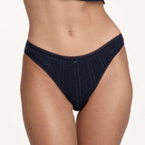 A close-up of a model wearing dark navy blue underwear with a lace trim, against a plain light background.