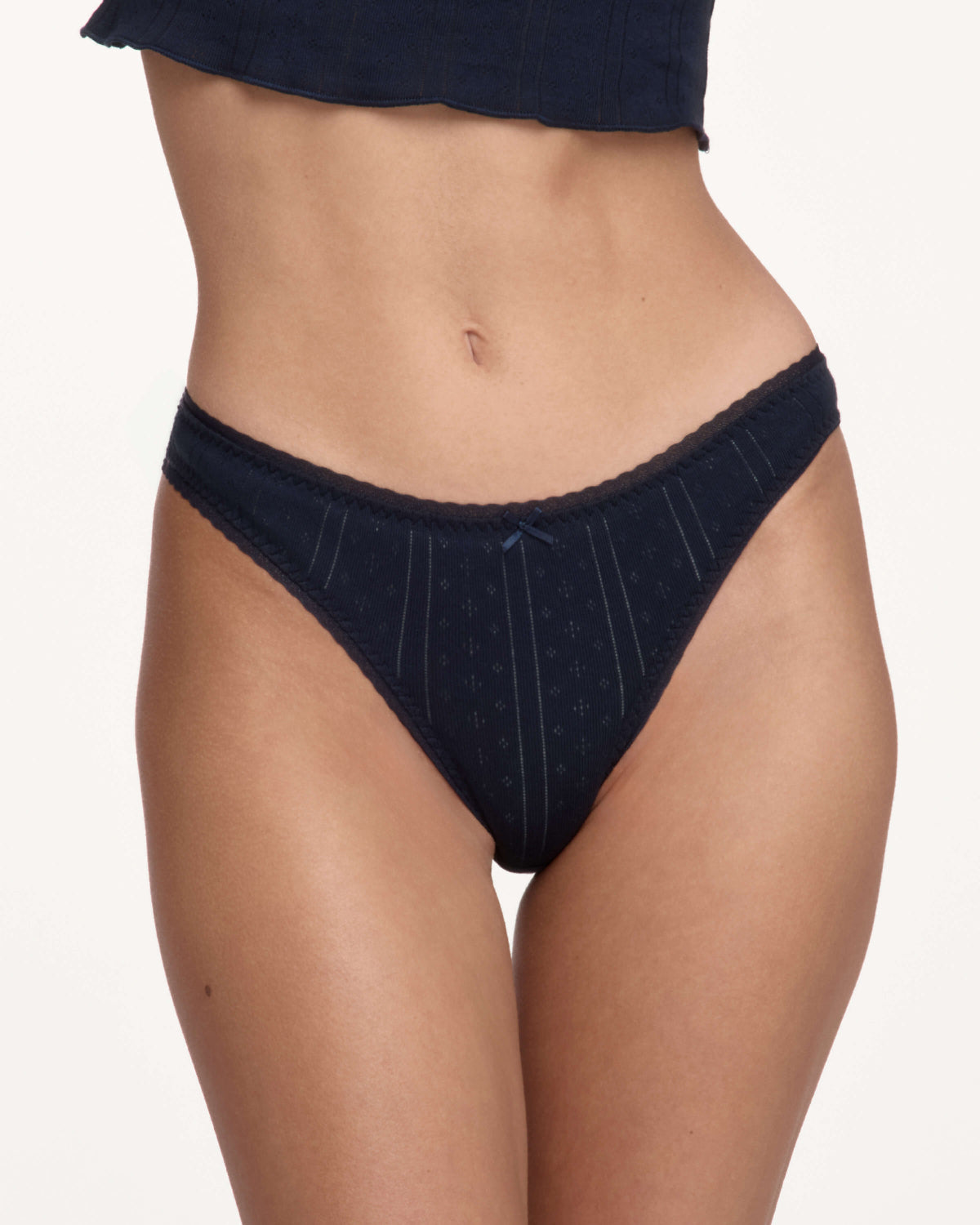 A close-up of a model wearing dark navy blue underwear with a lace trim, against a plain light background.