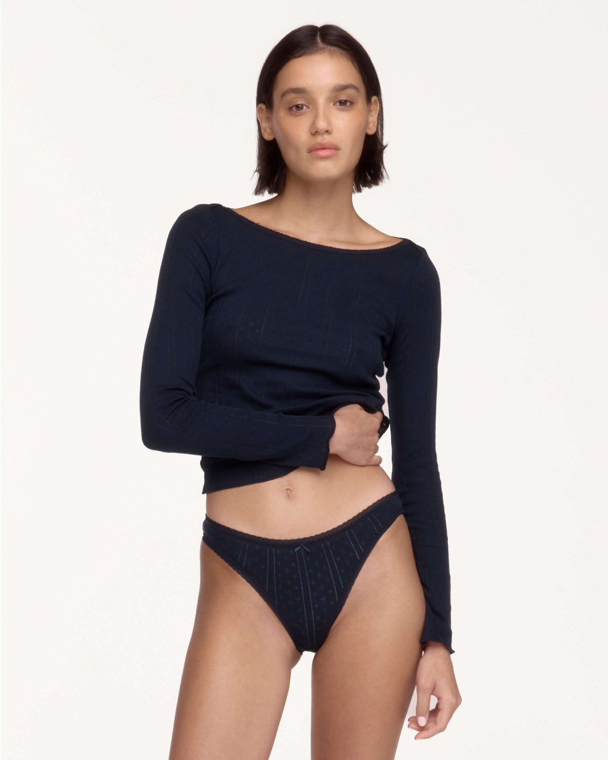 A model wearing a dark navy blue long-sleeve ribbed knit top and matching dark navy underwear, posed against a solid off-white studio background.