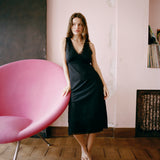 Woman in a black dress standing next to a pink chair in a room with a pink wall.