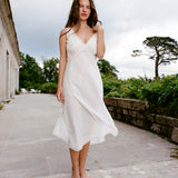 Woman in a white dress standing on a stone path with greenery and a building in the background