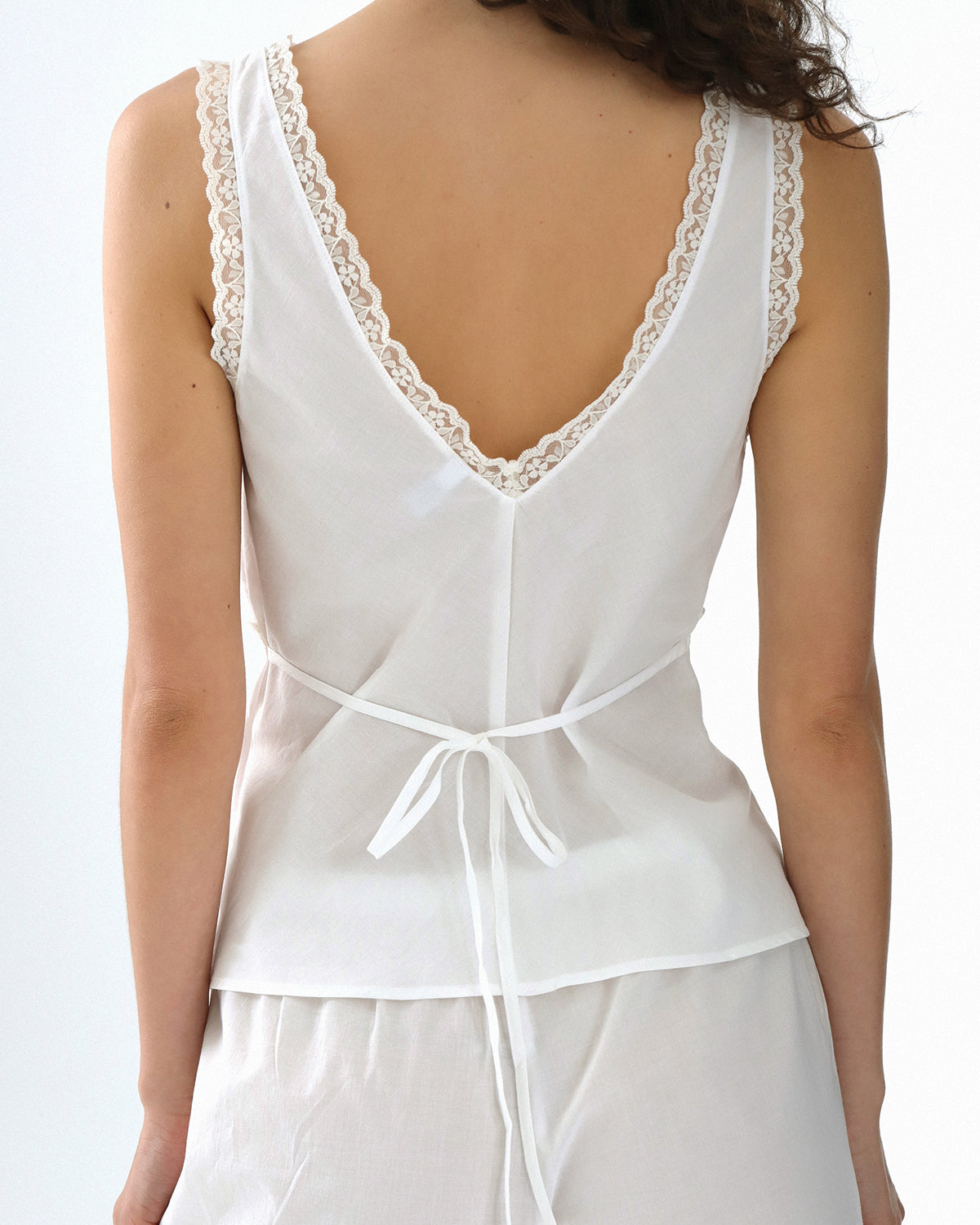 White lace-trimmed top worn by a person on a white background