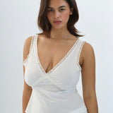 Woman wearing a white lace-trimmed top against a plain background