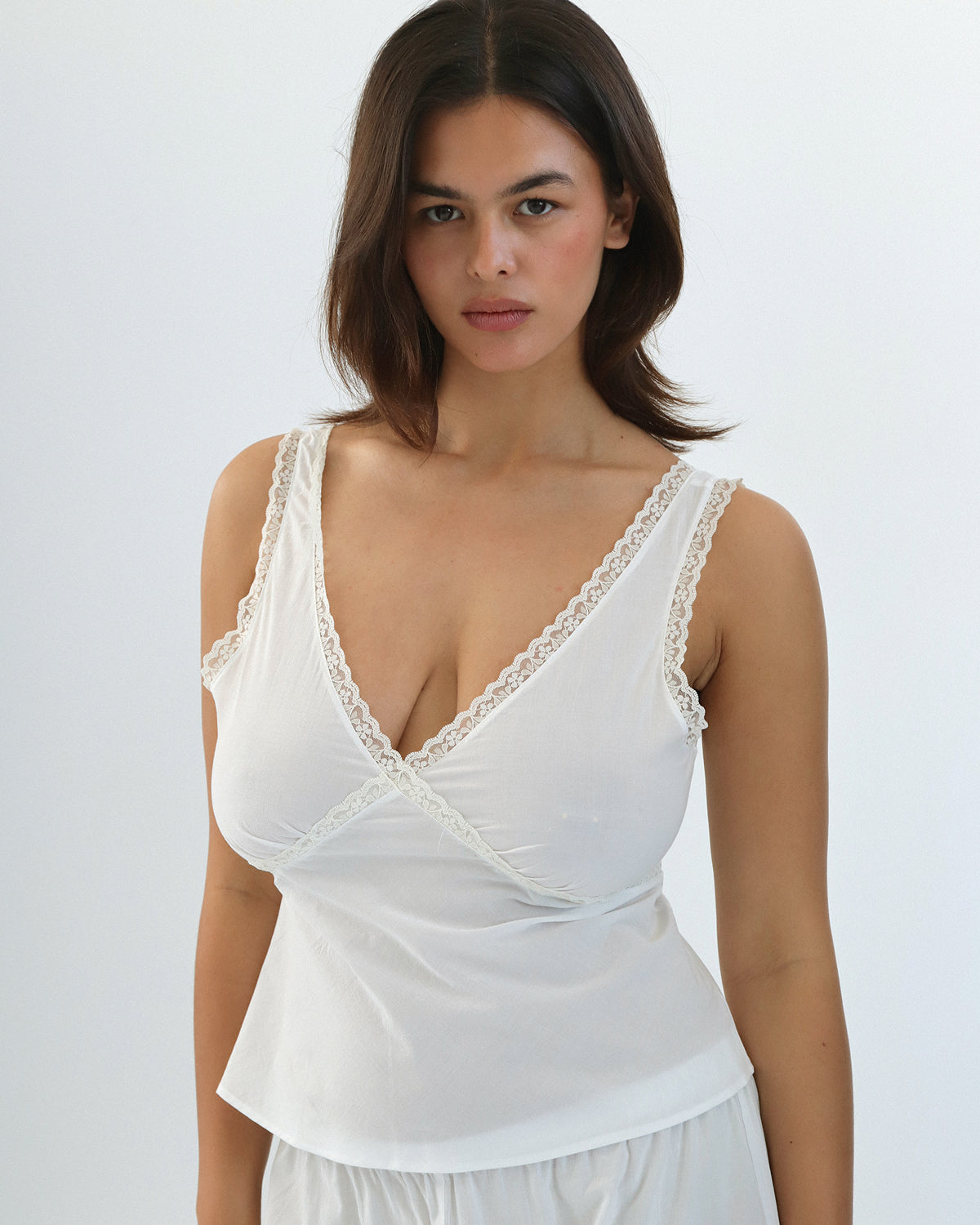 Woman wearing a white lace-trimmed top against a plain background