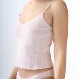 Woman wearing a light pink top and matching underwear against a plain background