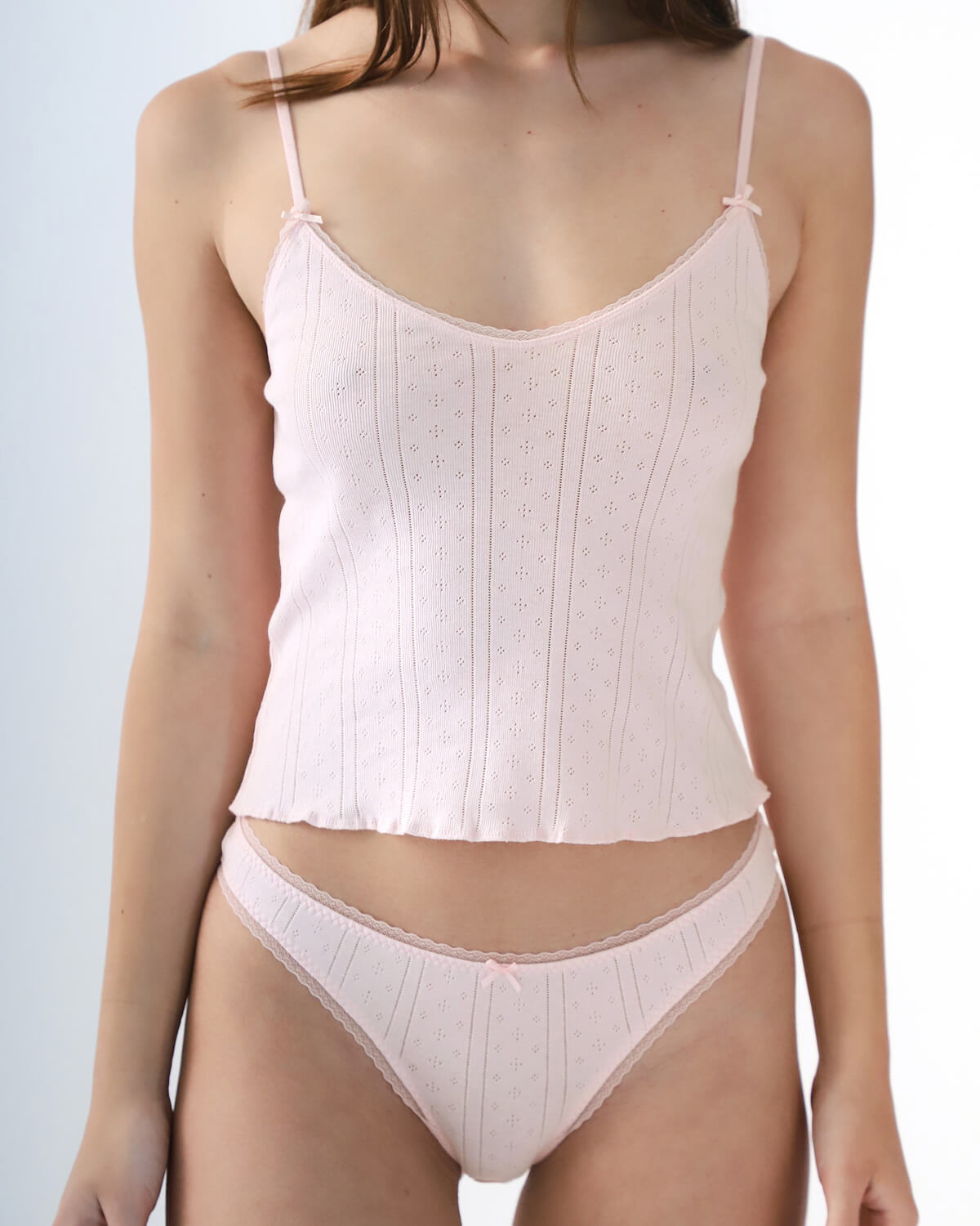 Woman wearing a light pink top and underwear set on a plain background