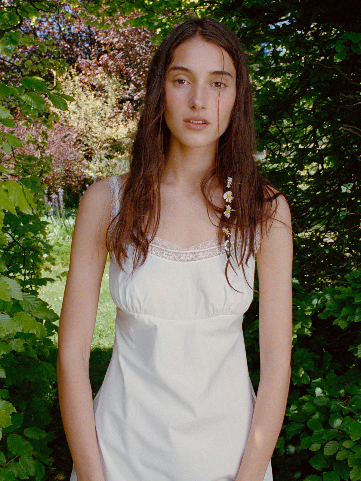 Woman in a white dress standing in a garden with greenery