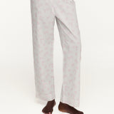 A person wearing white pajama pants with a small pink repeating pattern, shown from the waist down against a plain white studio background.