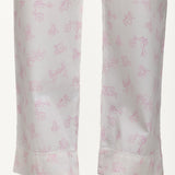 Close-up of a pair of white trousers with a delicate pink whimsical pattern and a lace trimmed hem, shown on a model's legs.