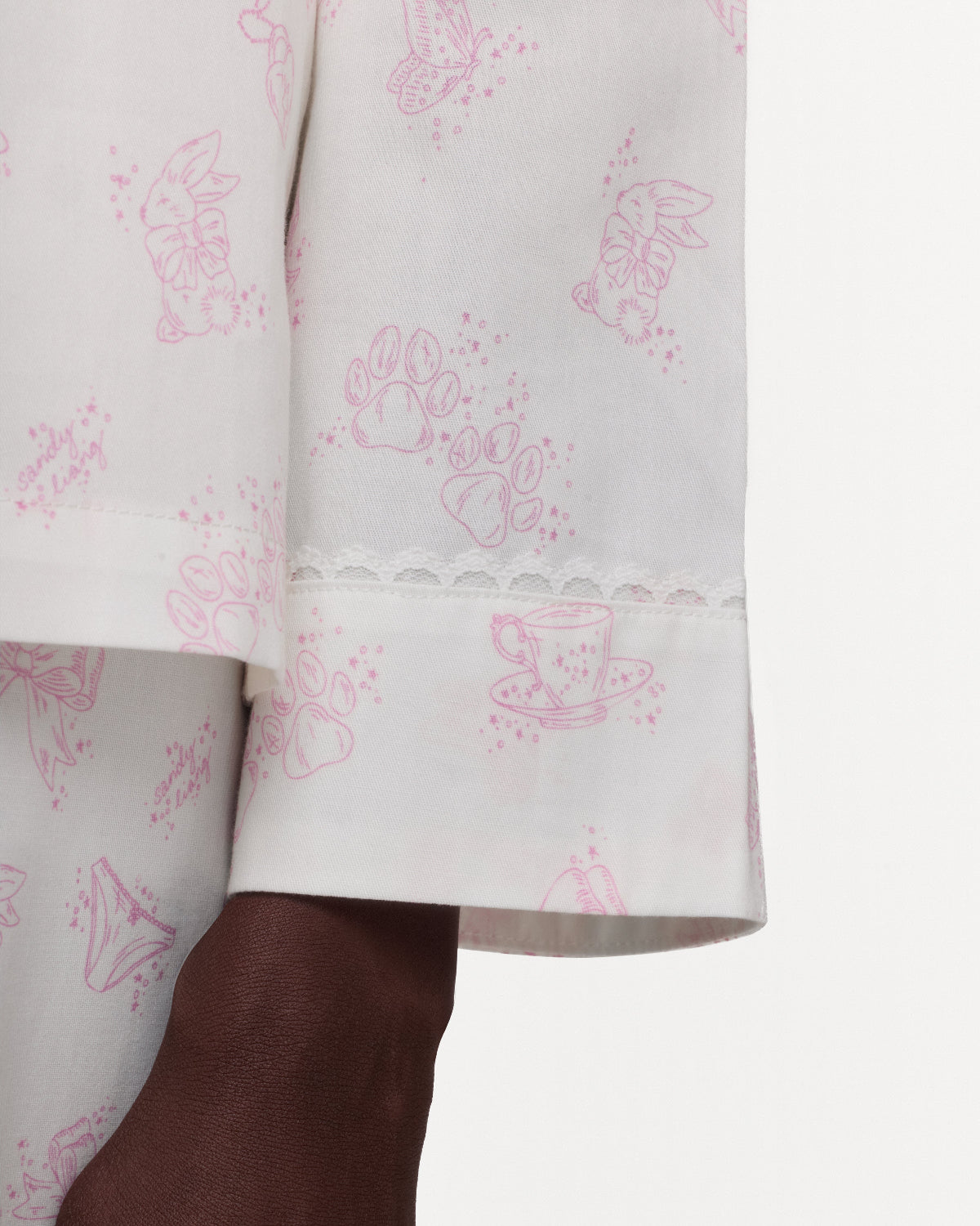 Close-up of a white pajama shirt with a pink bunny and teacup print, finished with a scalloped lace hem, shown on a model against a plain white background.