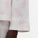 Close-up of a white pajama shirt with a pink bunny and teacup print, finished with a scalloped lace hem, shown on a model against a plain white background.