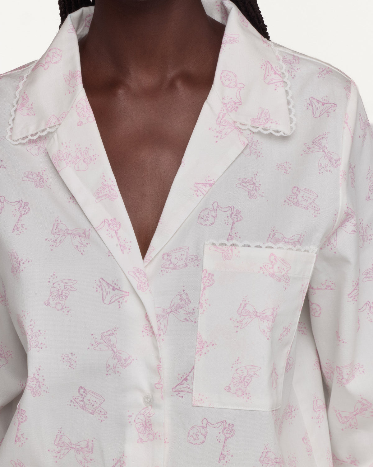 A close-up of a person wearing a white button-front shirt with a delicate pink allover print and scalloped collar and pocket edges.