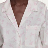 A close-up of a person wearing a white button-front shirt with a delicate pink allover print and scalloped collar and pocket edges.